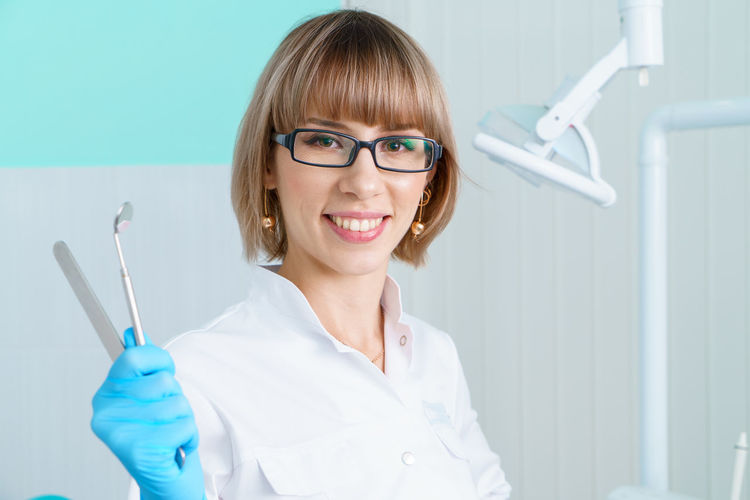 Woman dentist holding tools on background of the dental office in a white coat