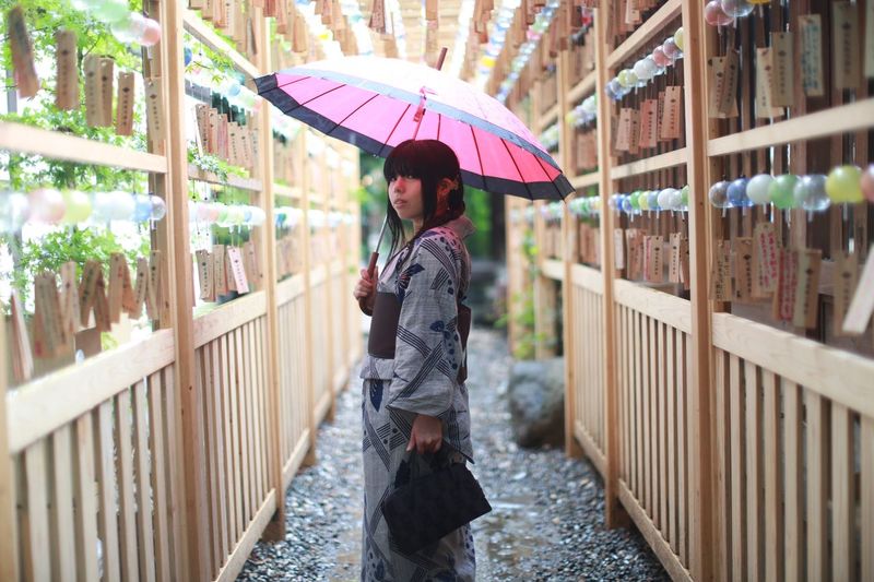 Side view portrait of young woman holding umbrella amidst wooden structure