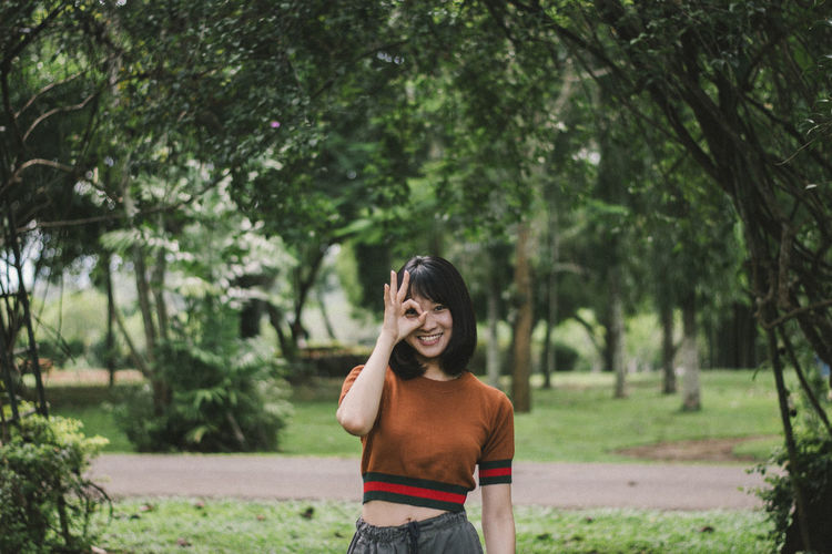 Portrait of smiling young woman gesturing while standing at park