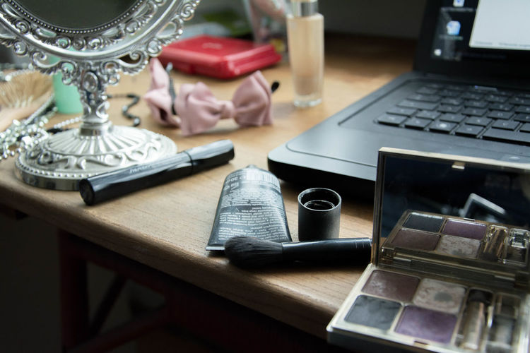 Close-up of cropped laptop and make up products on table