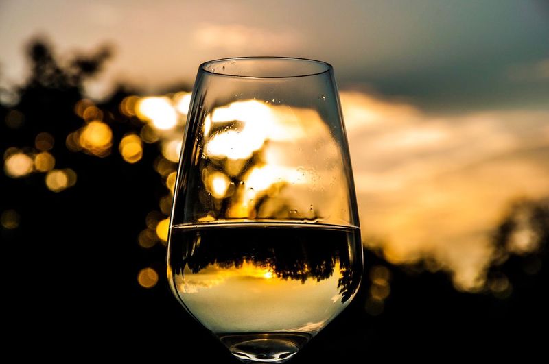 Close-up of drink in wineglass against sky during sunset