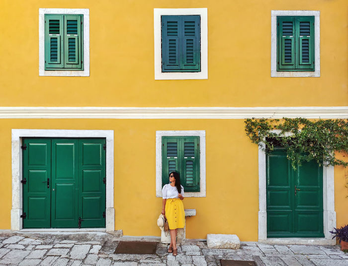 Young woman in summer outfit standing in front of yellow house.