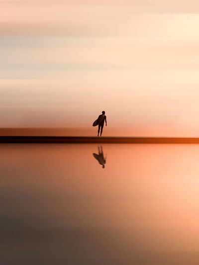 silhouette man standing on sea against sky during sunset