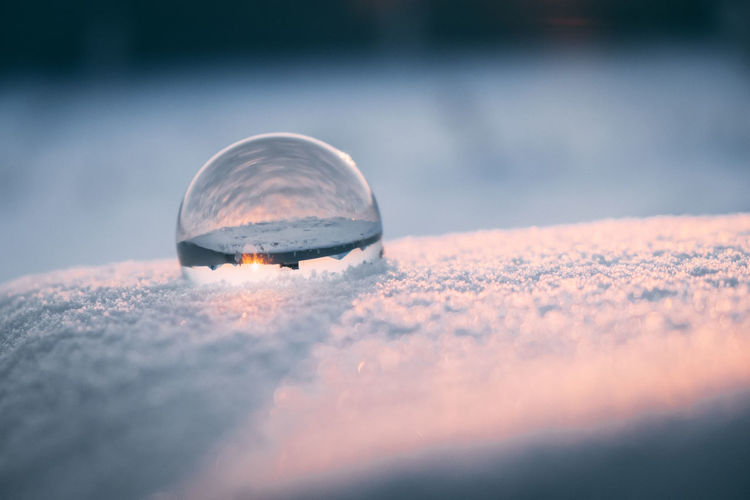 Glass transparent ball in the snow in winter, sun rays reflection. severe frost, cold