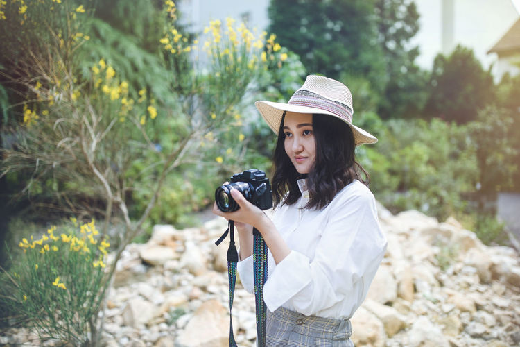 Young woman photographing with camera while standing outdoors