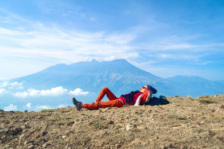 Side view of woman lying on mountain against sky