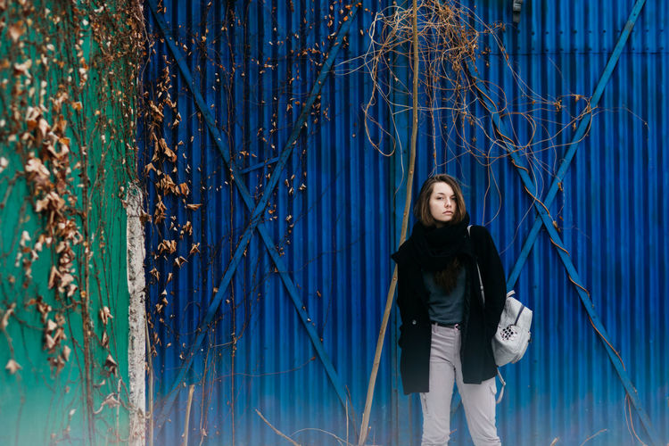 Portrait of young woman standing against blue corrugated iron