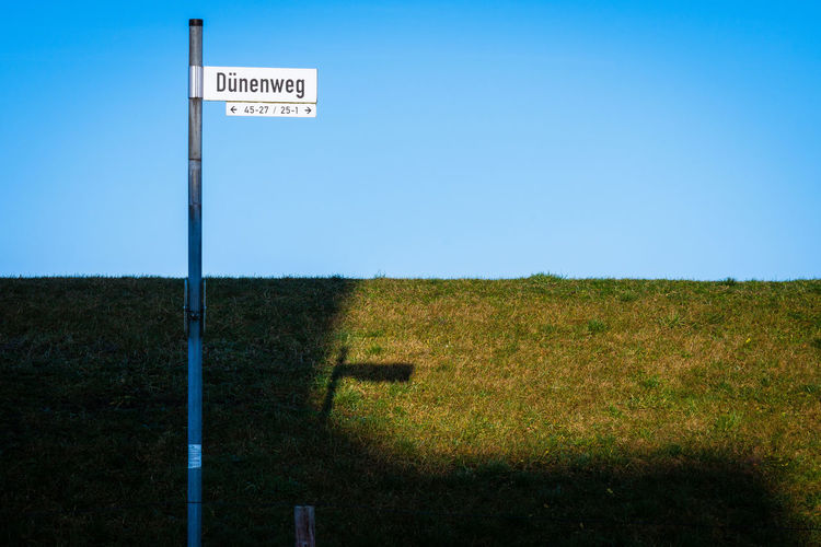 Road sign on field against clear sky