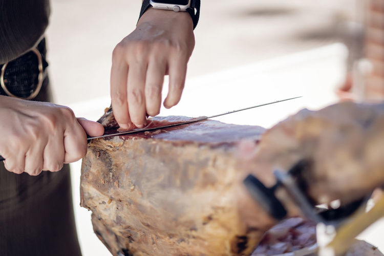 Woman cutting iberian pork ham with a ham holder and knife