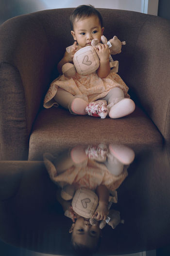 Cute baby girl holding soft toy while sitting on sofa at home