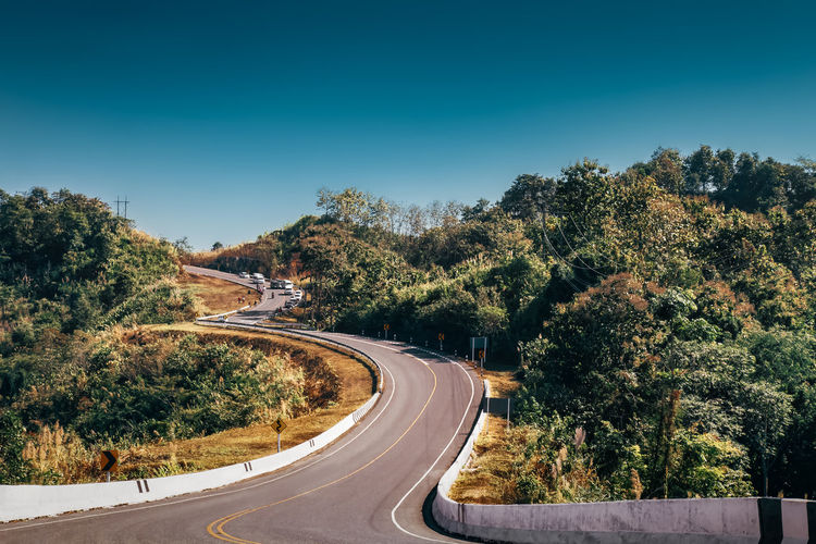 Road amidst trees against clear blue sky