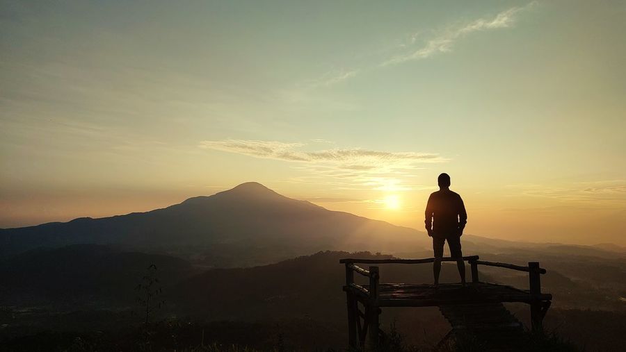 Rear view of man standing on mountain against sky during sunrise
