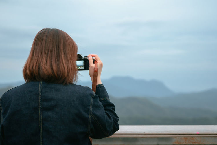Solo asian woman hipster traveler taking photo to mountain at outdoor bar of coffeeshop