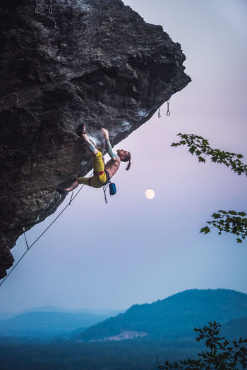 Man climbing overhanging sport climbing route with moon.