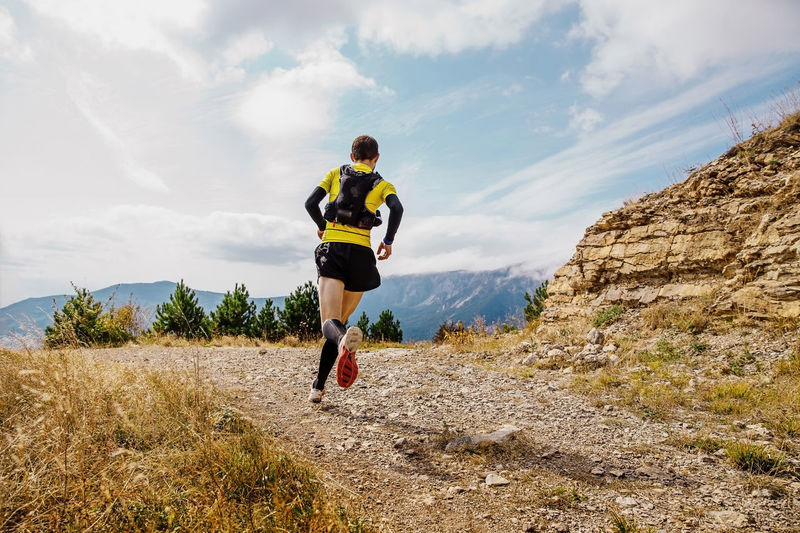 Rear view of man running mountain against sky