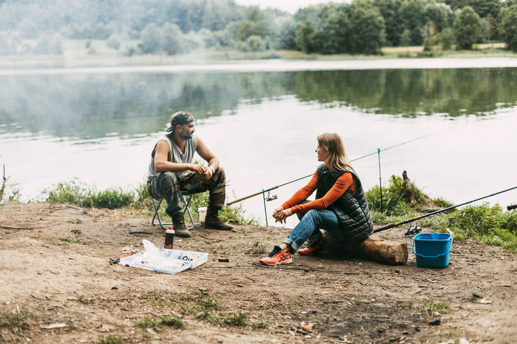 A man and a woman are fishing on the shore of a lake or river. a married couple spends time together