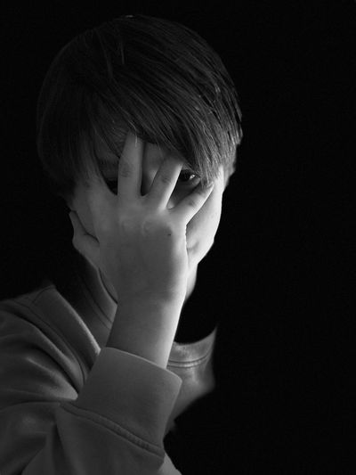 Close-up of teenage boy covering face against black background