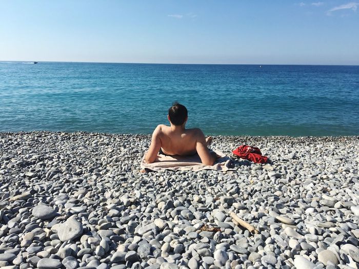 Full length of man sitting on pebbles at beach against sky