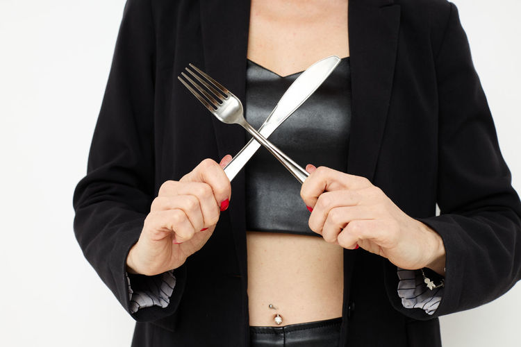Midsection of woman holding fork and knife against white background
