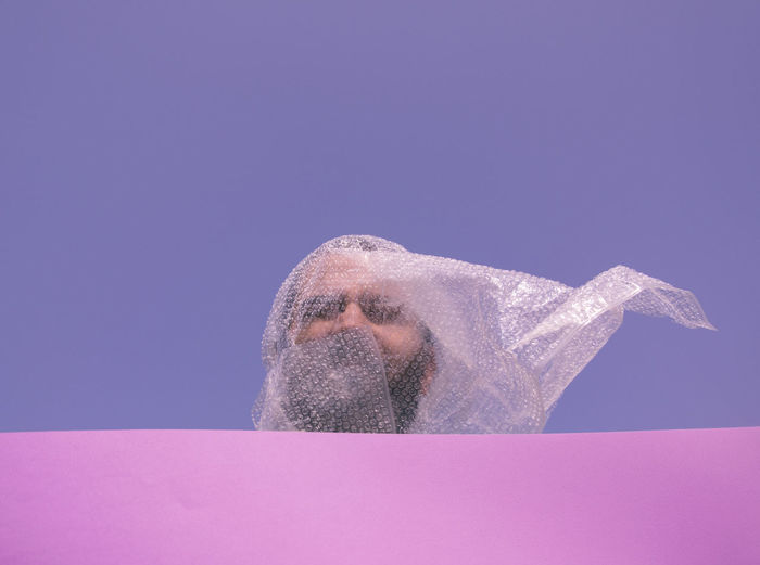 Low angle view of young man with bubble wrap standing against clear sky