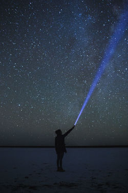 Full length of woman with flashlight standing against star field at night