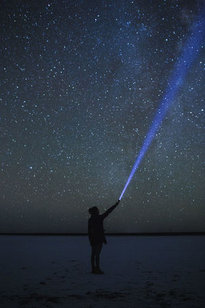 Full length of woman with flashlight standing against star field at night