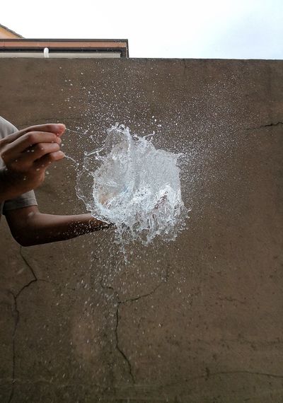 Cropped hands of person exploding water bomb against wall
