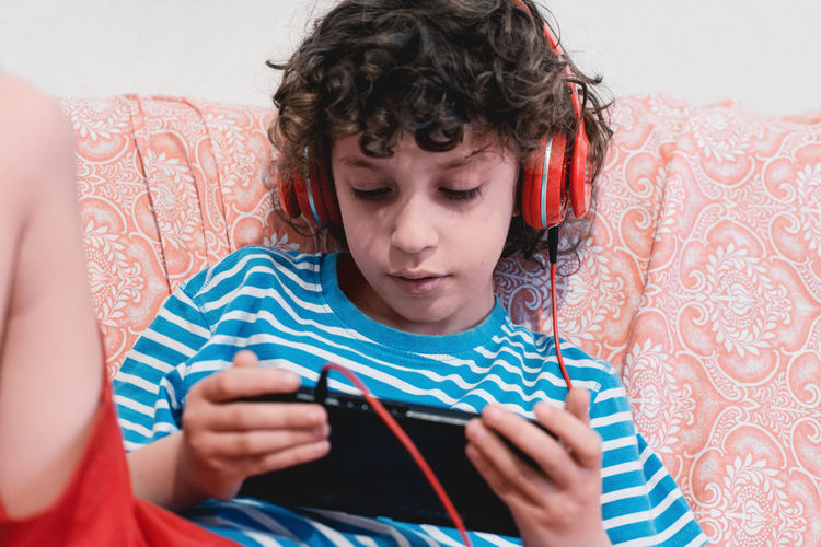 Boy using mobile phone while wearing headphones at home