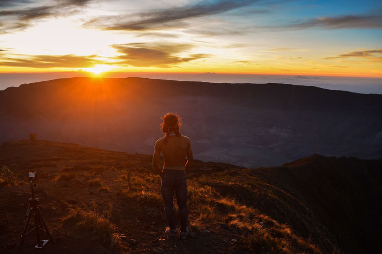 Rear view of shirtless man standing on mountain against sky during sunset