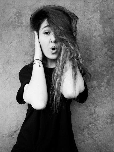 Portrait of woman with hands covering ears standing against wall