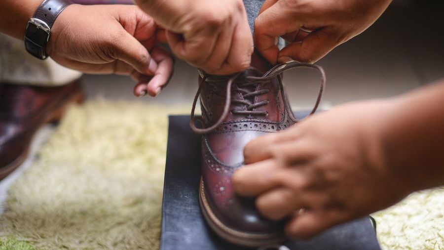 Cropped hands assisting man in tying shoelace