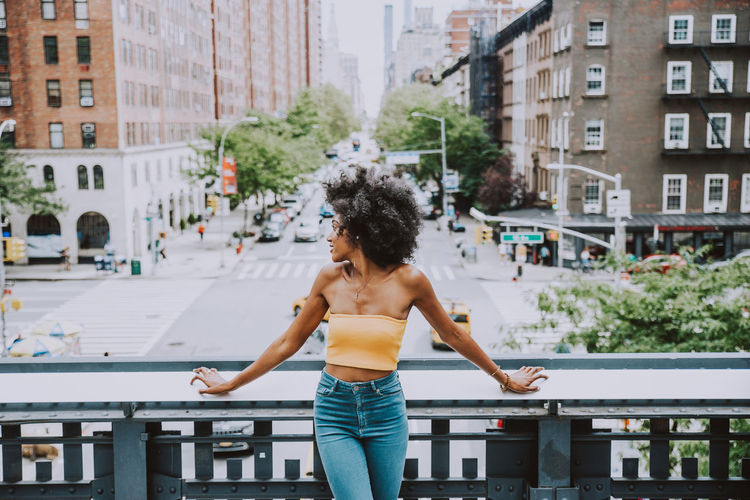 Young woman with afro hairstyle standing on bridge against city street