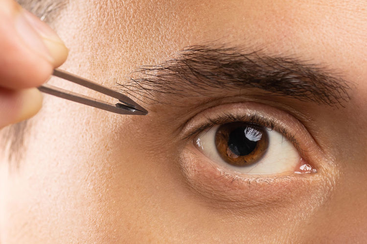 Male eye and tweezers for eyebrow shape correction