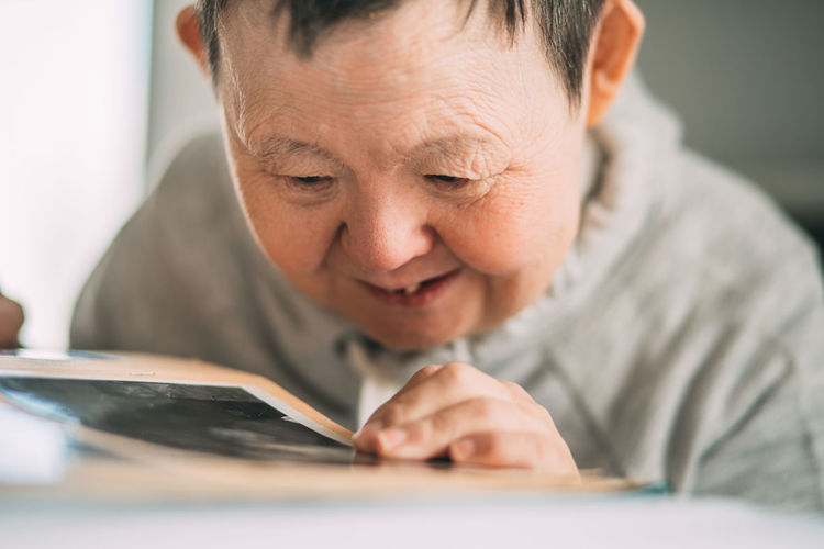 Smiling elderly woman with down syndrome looks at photos in an old album. save memory