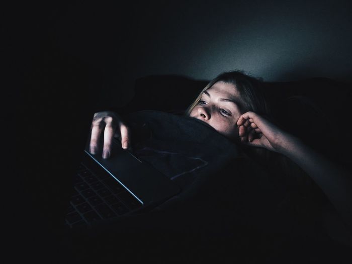 Young woman using laptop while lying on bed in darkroom