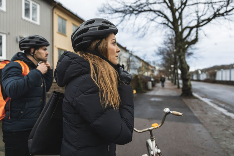 Heterosexual couple wearing cycling helmet at sidewalk in city