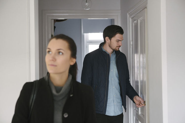 Young man looking at door while standing with woman in corridor