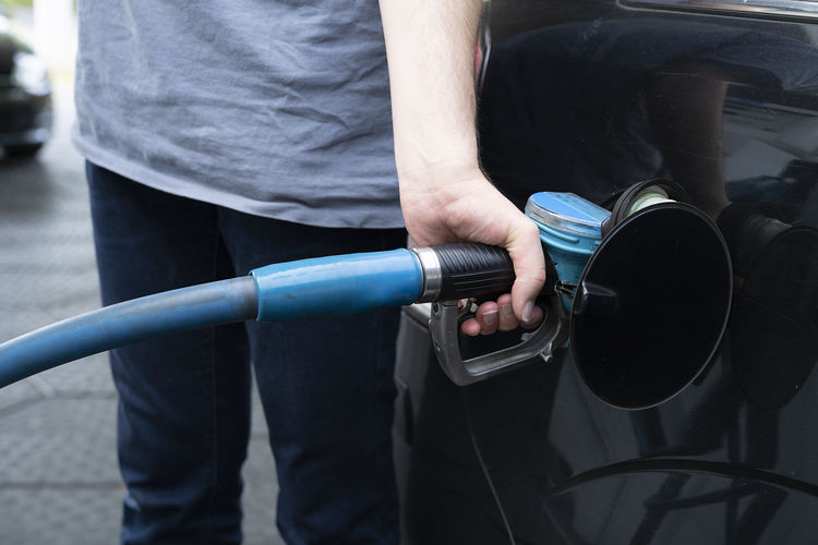 A male hand fills car with gasoline at the gas station holding a gaspump nozzle
