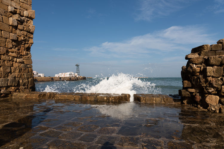 Sea waves splashing on rocks against sky