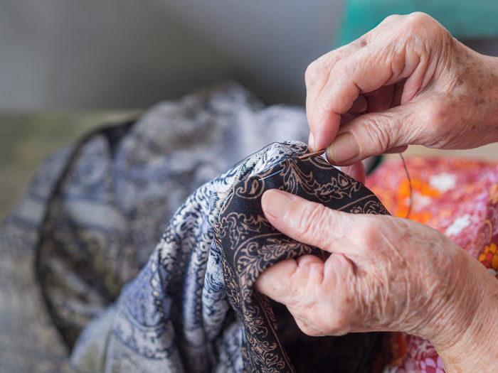 Close-up of elderly woman hands using needle and thread to mend a pants.