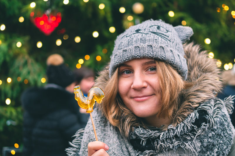 Portrait of smiling young woman holding candy against christmas tree