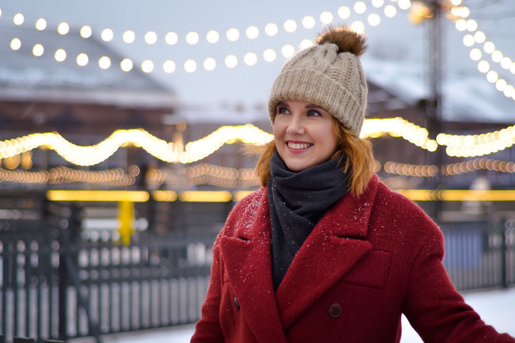 Portrait of smiling young woman standing at amusement park during winter
