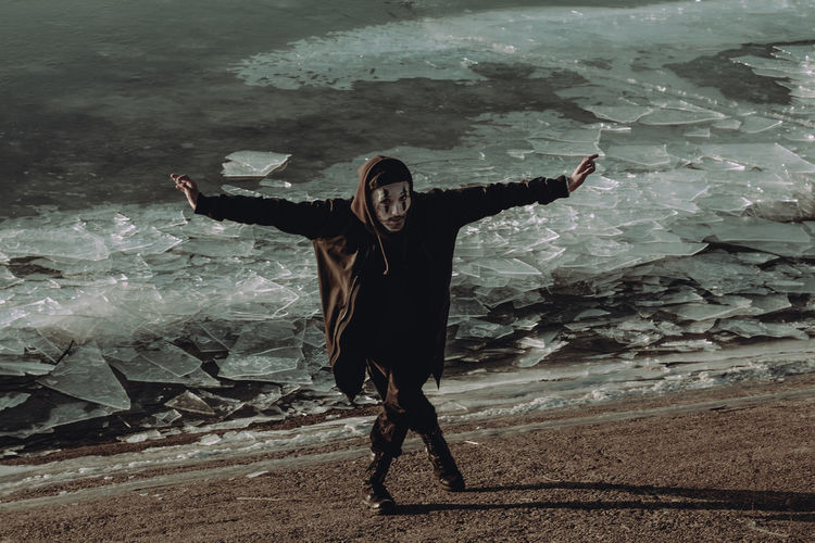 Young man with arms outstretched standing against frozen sea