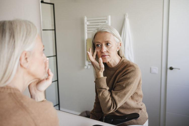 Woman applying moisturizer on face in bathroom