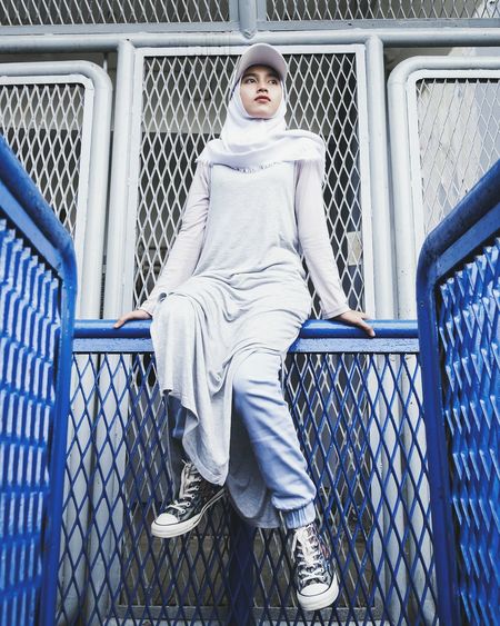 Low angle view of woman wearing hijab sitting on railing