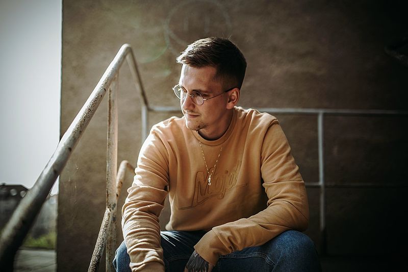 Young man looking away while sitting against wall