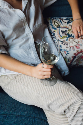 Casual elegant woman holding glass of white wine on couch