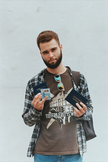 Portrait of young man holding id card while standing against wall