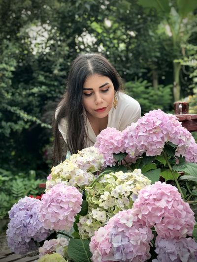 Beautiful young woman with pink flowers against plants