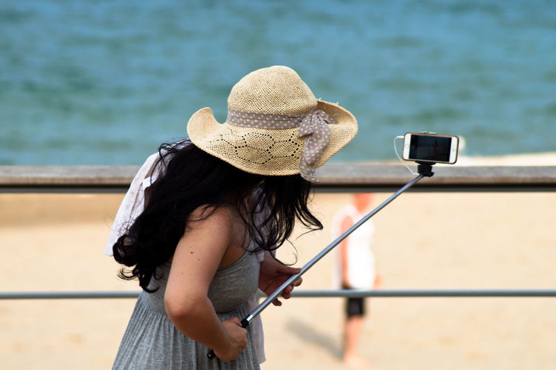 Side view of woman taking selfie with monopod at beach